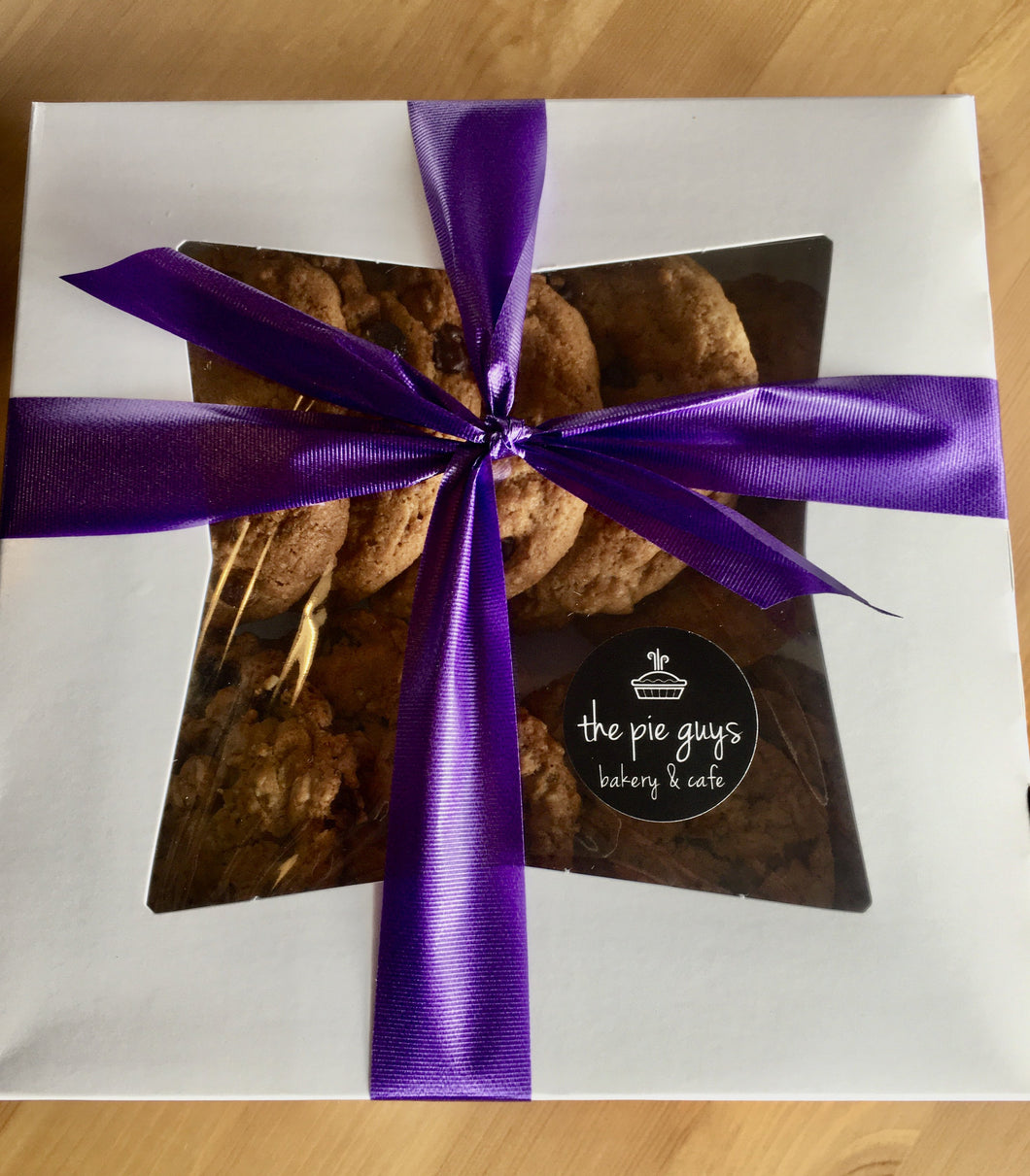 White box full of mixed cookies decorated with purple bow and official company sticker