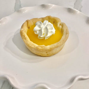 Single lemon tart on decorative tray with whip cream on top