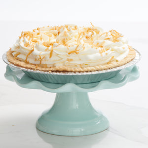 Coconut cream pie topped with whip cream and coconut placed on decorative stand