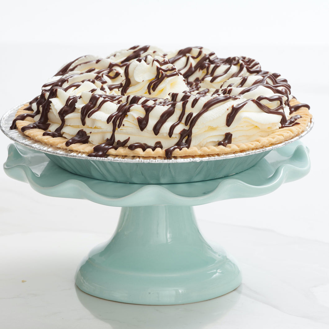 Chocolate cream pie covered in whip cream with dark chocolate drizzle placed on decorative stand
